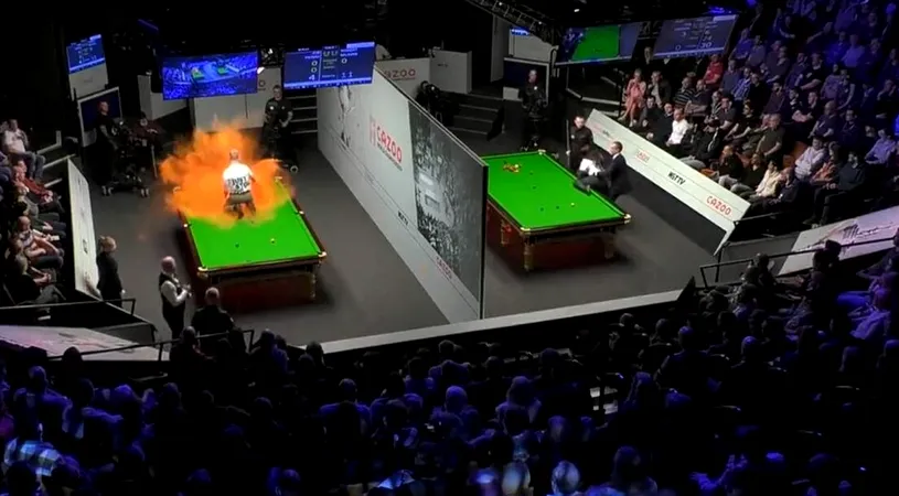 Scene halucinante la Campionatul Mondial de snooker! Așa ceva nu s-a mai întâmplat! Un protestatar s-a urcat pe masă în timpul meciului și a distrus-o după ce a împrăștiat un praf portocaliu! La masa alăturată s-a încercat același gest extrem! VIDEO